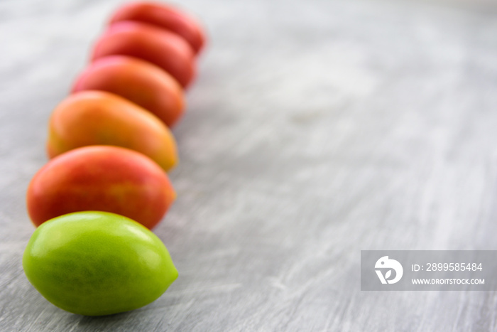 Green, yellow and red plum tomatoes in row