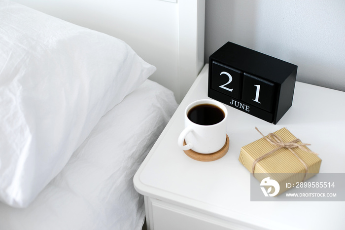 Morning cup of coffee, gift present, black wooden calendar on bedside table on Happy Fathers Day. Holiday concept