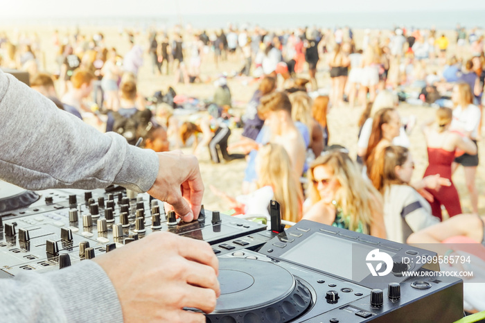 Close up of DJ’s hand playing music at turntable at beach party festival - Crowd people dancing and having fun in club outdoor - Concept of youth summer party lifestyle