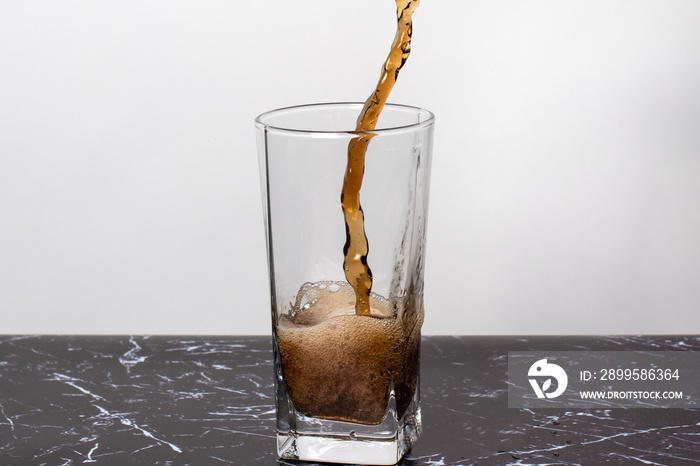 A brown dark sweet drink is poured into a glass beaker, spatter and a splash of beverage.