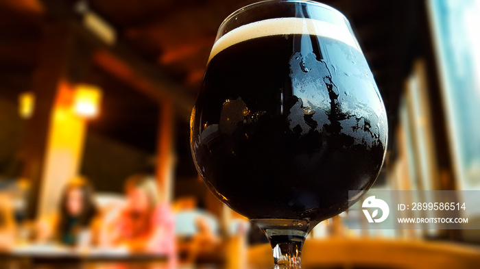 Glass of fresh dark beer on rustic pub background