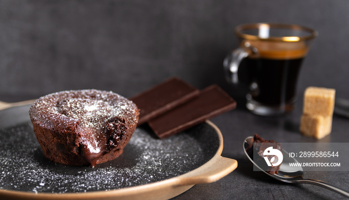 Warm chocolate lava cake on a black plate with a cup of coffee on a dark background