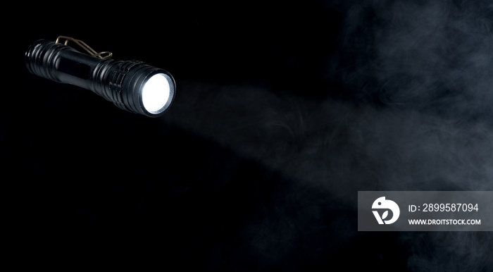 Flashlight with a light beam on dark smoke background