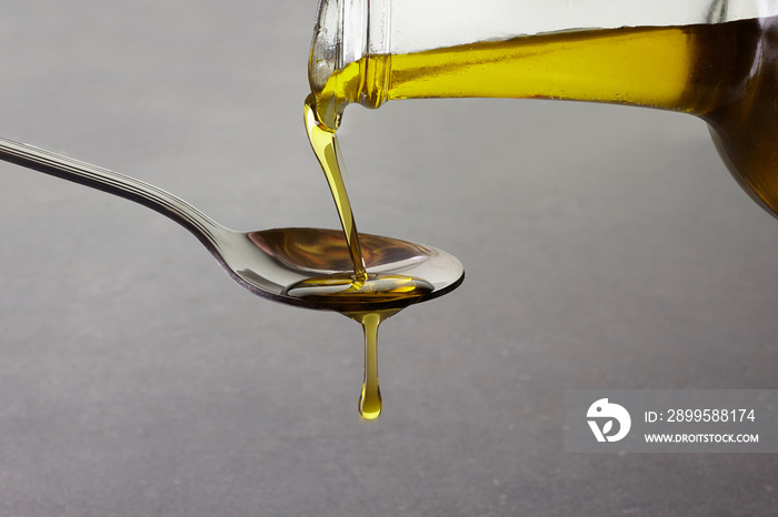pouring olive oil from glass bottle on grey background
