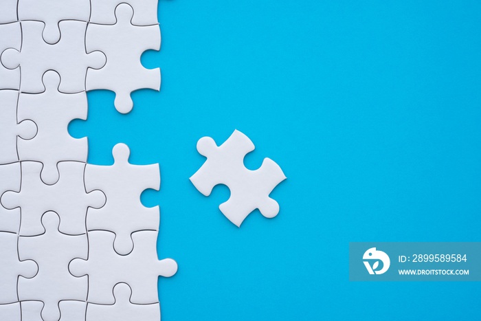 Unfinished white jigsaw puzzle on blue background with copy space. Business strategy teamwork and problem solving concept. Teamwork is collaborative effort of team to achieve goal or to complete task.