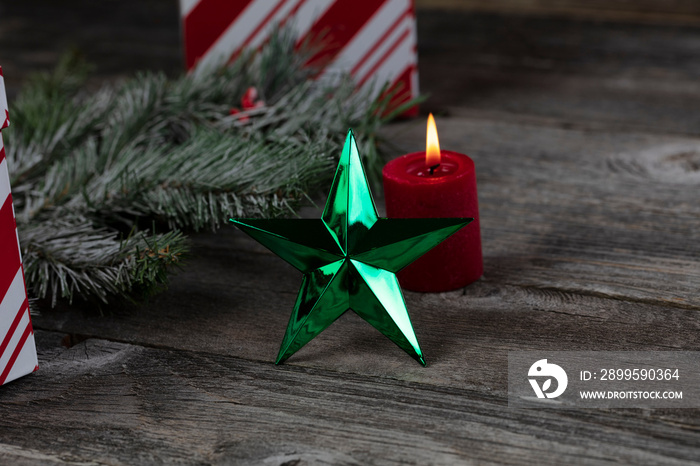 Bright green star ornament and burning candle, gift box plus snow fir branch decorations on rustic wooden planks for a merry Christmas or happy New Year holiday celebration concept