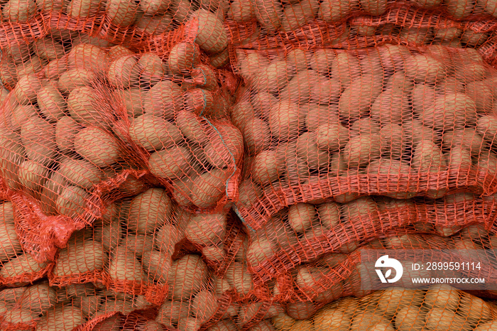 Red Potatoes in red burlap net sacks on the pallet at the market. Background raw food