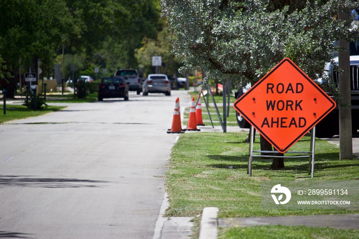 Road Work Ahead sign on metal a-frame stand with traffic cones behind