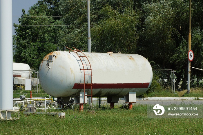 one large industrial iron white barrels with red staircase at a gas station stand on a green grass in the street