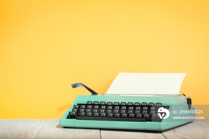 Retro old mint green typewriter with paper sheet on wooden table front yellow background. Vintage style filtered photo