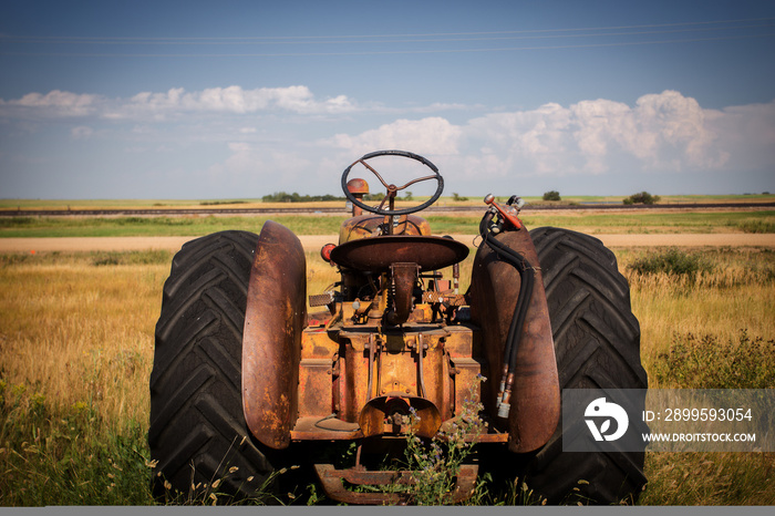 The back end of a rusted vintage tractor facing out toward fields under cloudy sky in a rural black and white summer countryside landscape