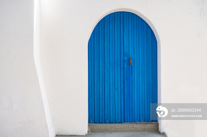 Blue wooden door on white house wall background front view. Greek island traditional architecture.