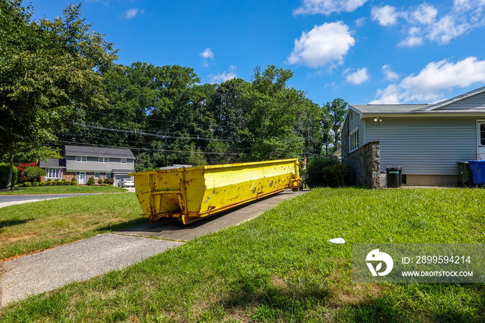 A bright yellow dumpster in the driveway of a home in a residential neighborhood