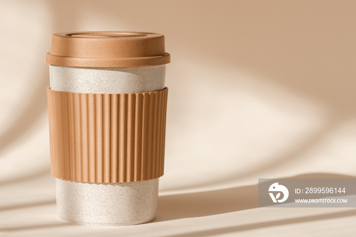 Sustainable bamboo eco friendly cup with silicone holder on natural shadow beige background. Reusable, biodegradable travel plastic coffee mug for take away. Zero waste, sustainability concept.