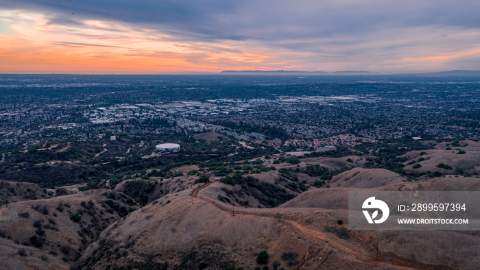 Aerial view of open rolling hills in suburban Southern California.  Radio tower atop hill during sunset surrounded by mountains and ocean