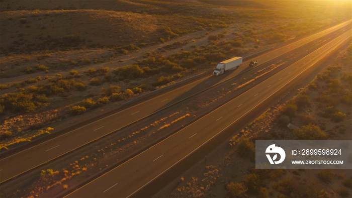 AERIAL: Cars and semi trucks driving on busy highway at summer sunset