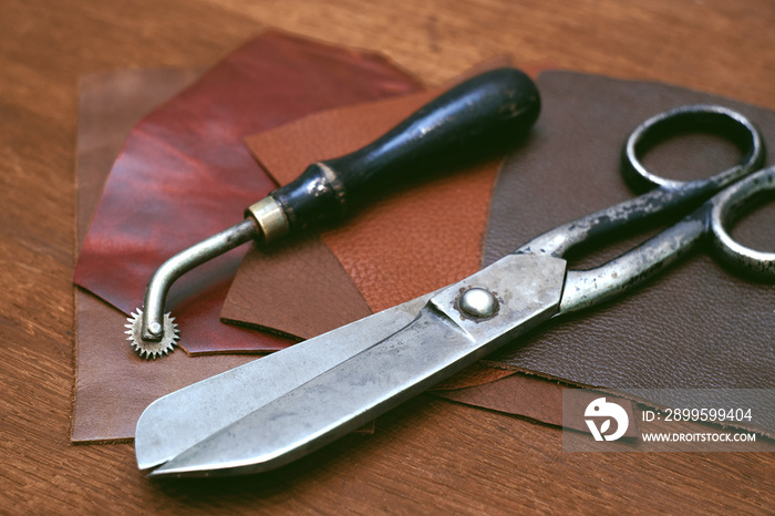 Large metal tailor scissors on a wooden table.Pieces of genuine leather for the manufacture of products. Shoe repair.