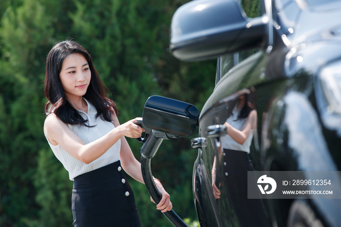 青年女人拿着充电枪准备给汽车充电