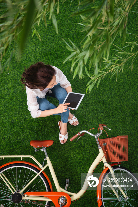坐在草地上使用平板电脑的青年女人