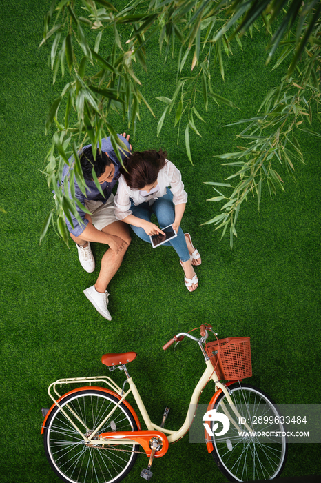 青年伴侣坐在草地上使用平板电脑