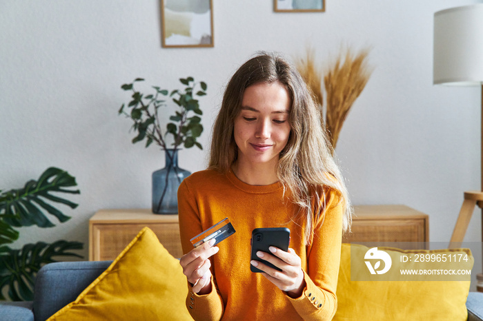 Happy woman shopping online with credit card and cell phone at home