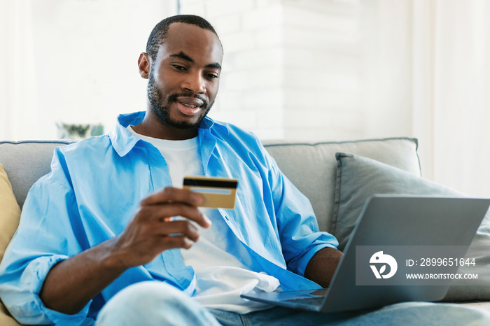 Fast online shopping. Portrait of black man holding credit card in hand and using laptop, making fin