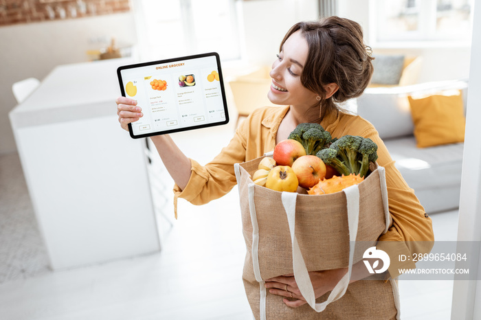 Happy woman holding a digital tablet with launched online store while standing with shopping bag ful