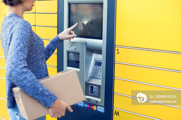 Woman using automated self service post terminal machine or locker to deposit the parcel for storage