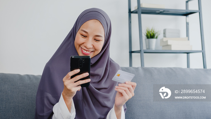 Asia muslim lady use smart phone, credit card buy and purchase e-commerce internet in living room at