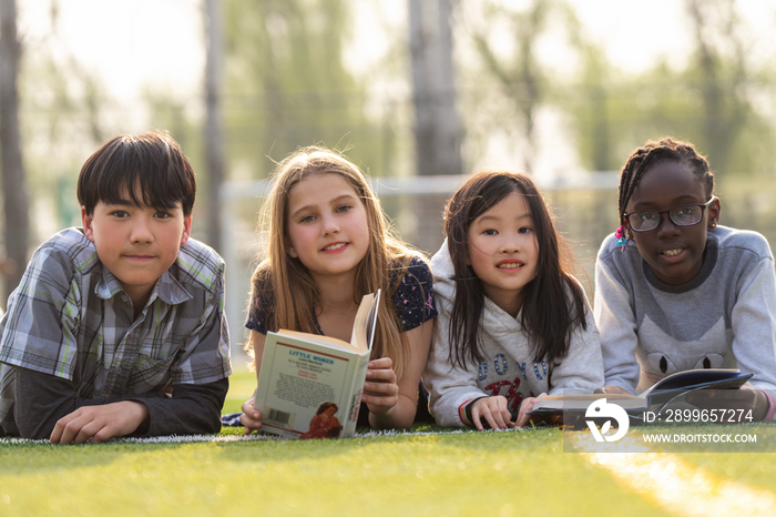 可爱的小学生们趴在草地上看书