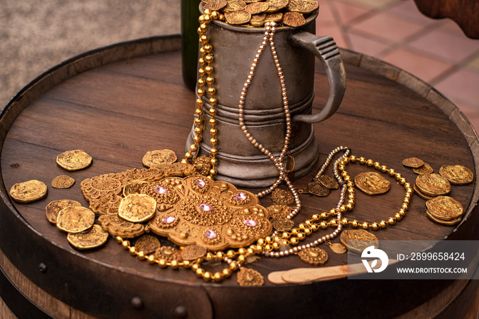 Artificial gold coins and a decoration on a wooden barrel. A filled mug with gold artificial coins.J