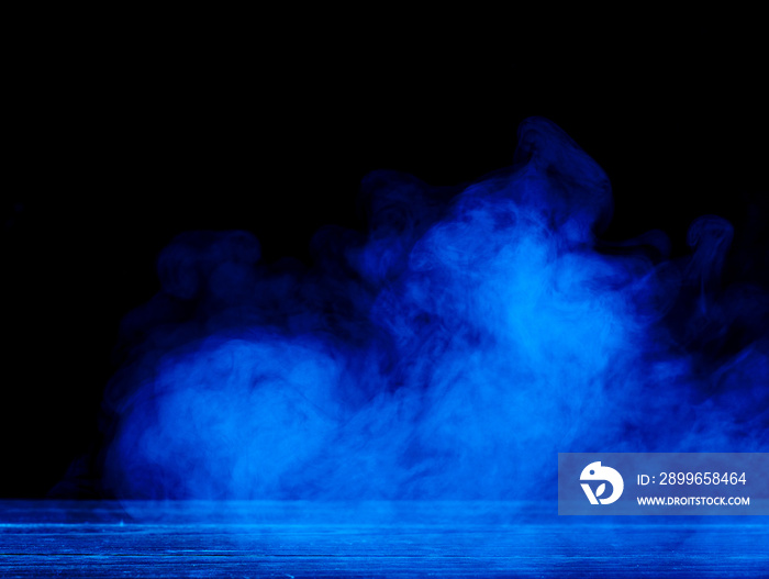 Conceptual image of blue smoke isolated on dark black background and wooden table.