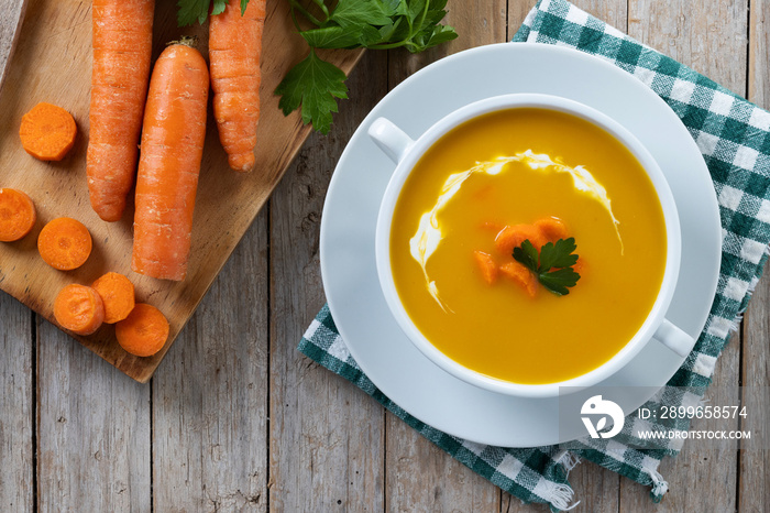 Carrot soup with cream and parsley on wooden table. Top view