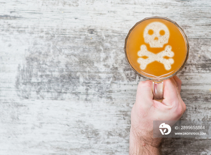 mans hand holds a mug of beer with with a skull and cross bones on a beer foam. Top view. Space for