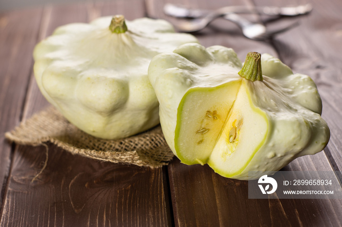 Group of two whole summer white pattypan squash one sliced on linen cloth on brown wood