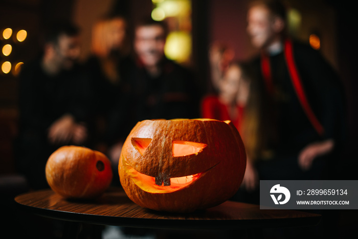 Halloween carved pumpkin on the table at the cafe. Against the background of a group of friends cele