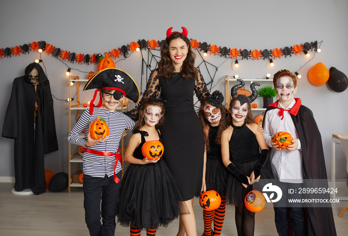 Portrait of happy teacher together with kids at Halloween party. Indoor shot of young woman and chil