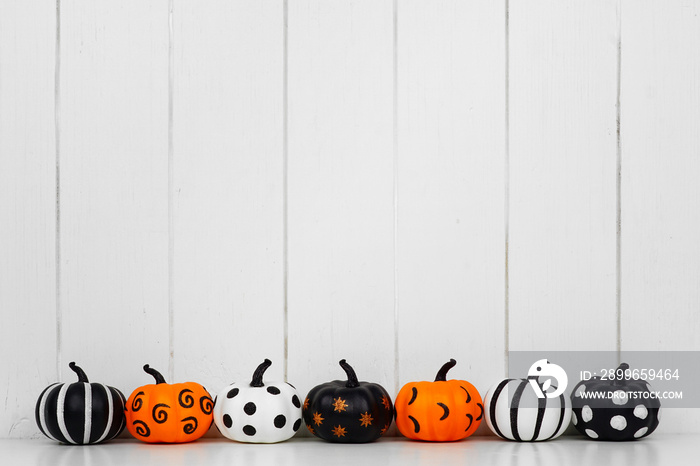 Black, white and orange patterned Halloween pumpkins in a row against a white wood background. Copy 