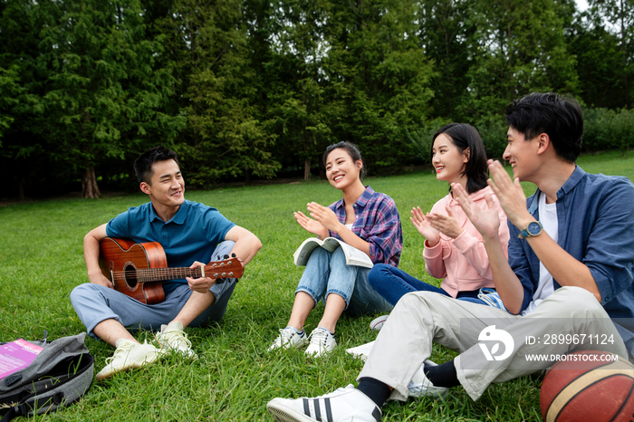 快乐的大学生在草地上弹吉他唱歌