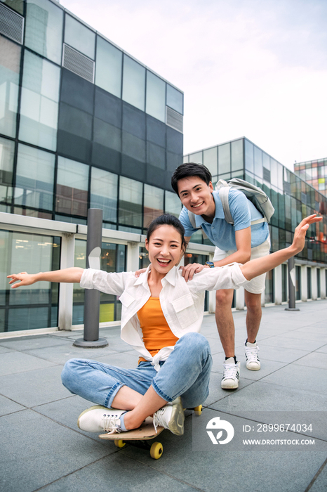 年轻男子向前推着坐在滑板上的女友