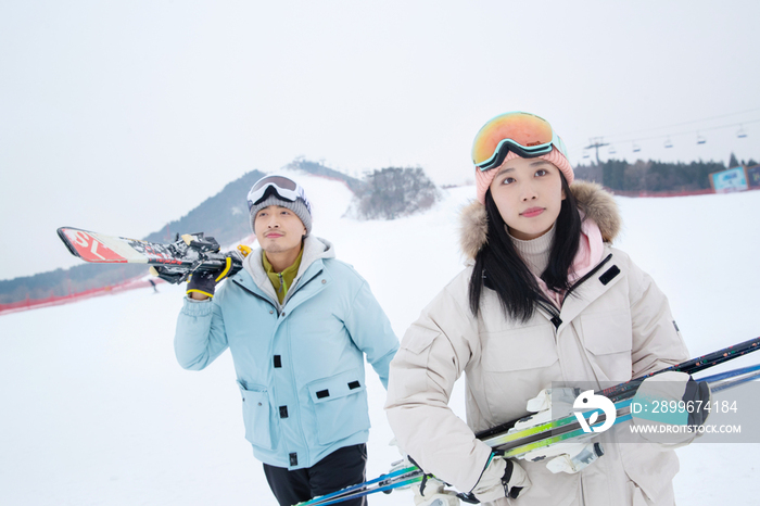 雪场上拿着滑雪板去滑雪的情侣