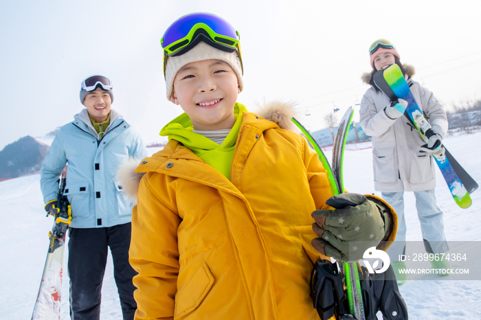 雪场上拿着滑雪板的一家三口