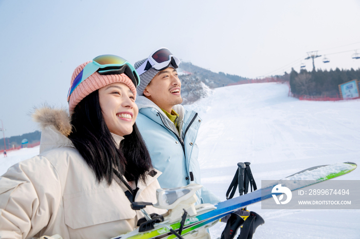 雪场上拿着滑雪板滑雪杖的快乐情侣