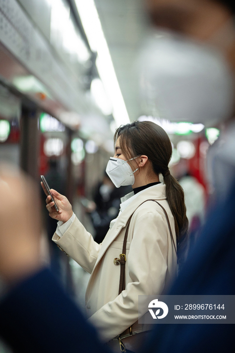 戴口罩的年轻女人在地铁里看手机