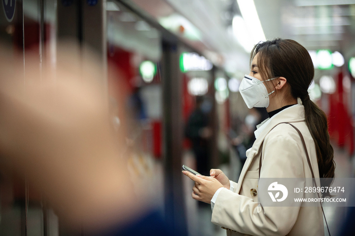 戴口罩的年轻女人站在地铁站台上