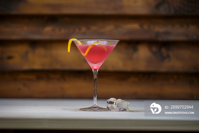 Fresh cosmopolitan martini with lemon twist on table with wood background