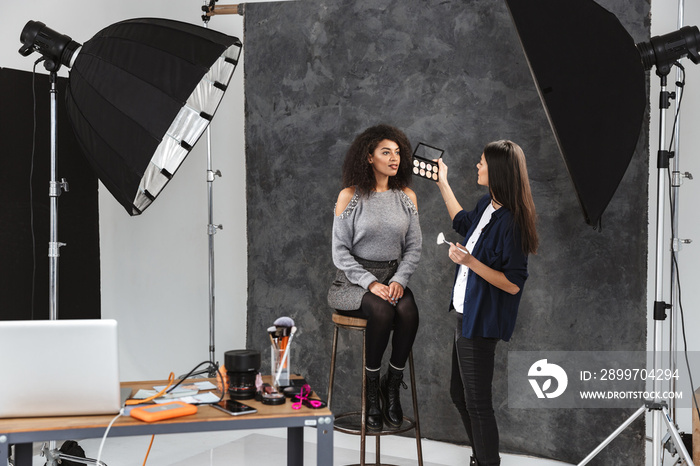 Portrait of female makeup artist applying professional cosmetics to african american woman during ph