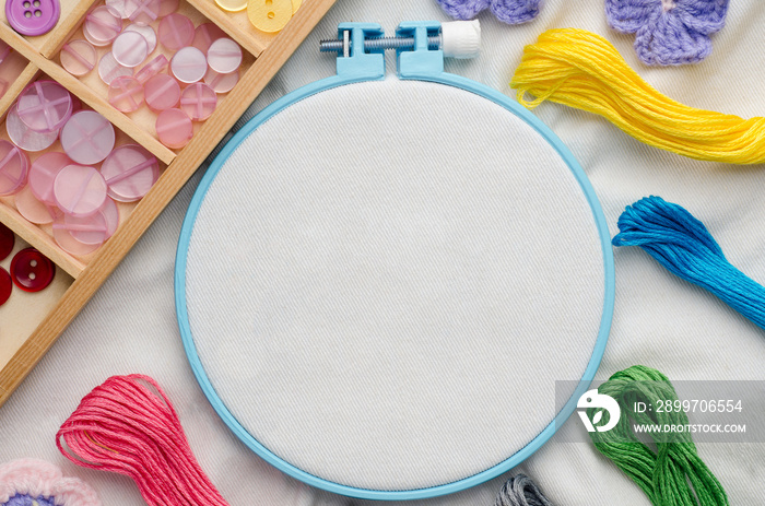 Embroidery hoop with blank fabric, colored sewing threads and va