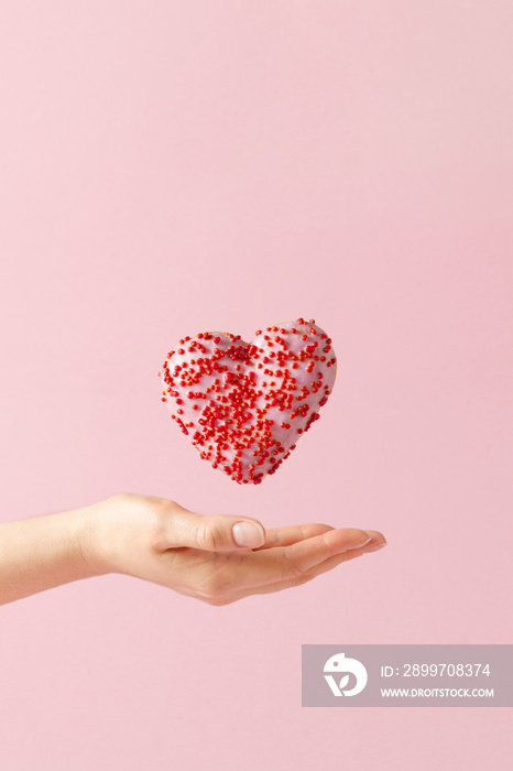 Heart shaped donut and women hand over pastel pink background.