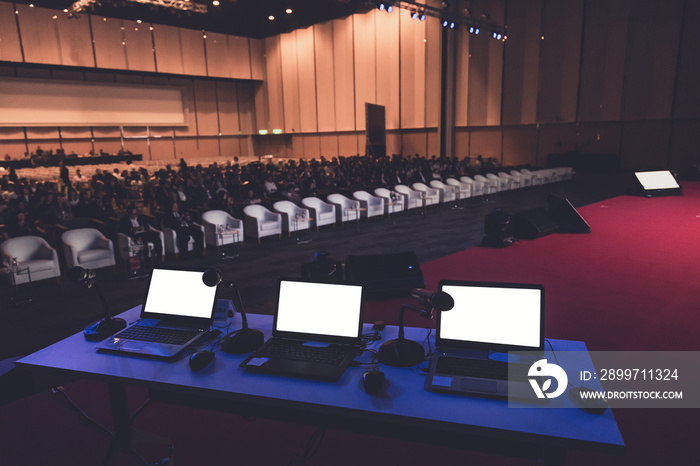 business laptop and microphotone at podium in seminar room with attendee background, Business meetin